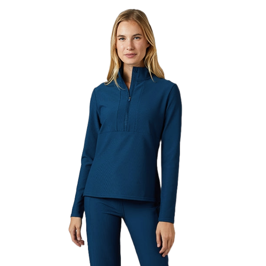 A woman is wearing a blue long-sleeve half-zip top and matching blue fitted pants, paired with white sneakers.