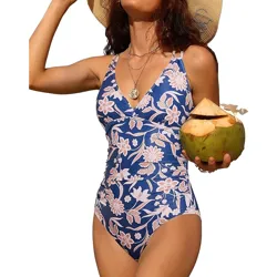 A woman in a blue floral one-piece swimsuit holds a coconut and wears a straw hat with layered necklaces.