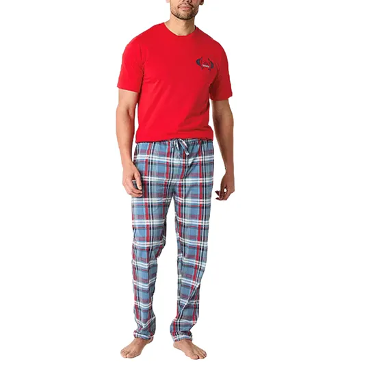 A man is wearing a red T-shirt and blue plaid pajama pants with a drawstring, standing barefoot.