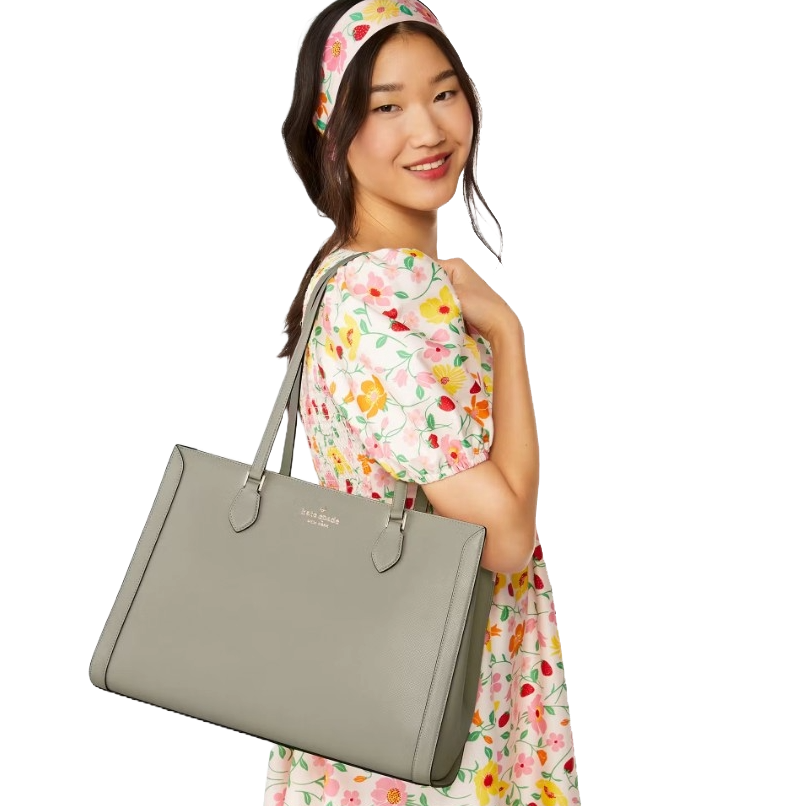 A woman with a floral dress and matching headband carries a gray Kate Spade tote bag on her shoulder.
