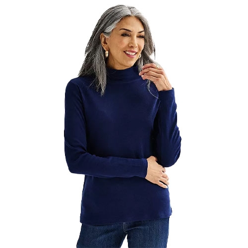 A woman with long gray hair is wearing a navy blue turtleneck sweater paired with jeans.