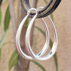 Silver teardrop hoop earrings hanging on a circular holder, reflecting light.