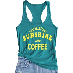 A teal racerback tank top with \“Sunshine and Coffee\“ printed in bold yellow lettering, paired with light blue denim shorts.