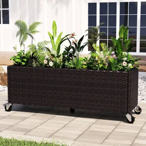 Rectangular wicker planter box on wheels, filled with various green plants and small white flowers, placed on a patio near a white building.