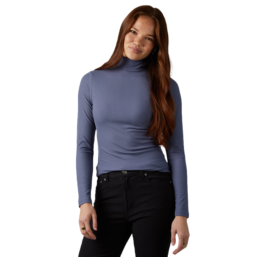 A woman is wearing a long-sleeve turtleneck top in a muted blue tone paired with high-waisted black jeans.
