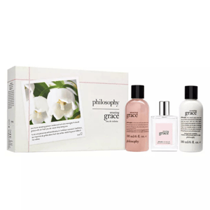 The 3pc Amazing Grace Gift Set includes a 6 oz shampoo and shower gel, a 6 oz firming body emulsion, and an eau de toilette spray, all featuring the Amazing Grace fragrance. The packaging includes white flowers and text about the product.