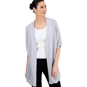 Woman wearing a light gray open-front cardigan with a diamond knit pattern over a white top and black pants.