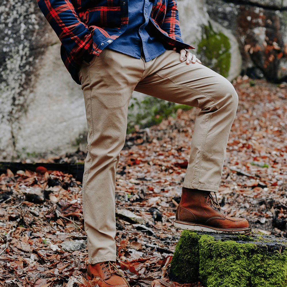 A person outdoors wearing khaki pants, brown leather boots, and a blue shirt with a red flannel jacket.