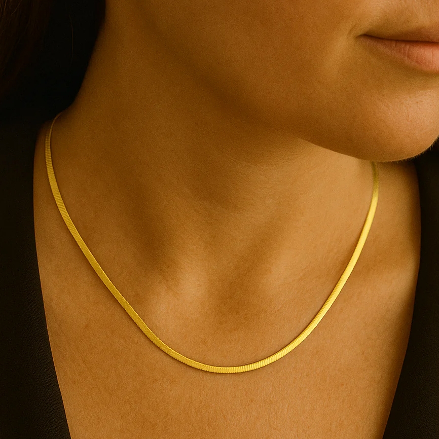A woman is wearing a sleek, thin gold necklace close to her neck, paired with a black outfit.