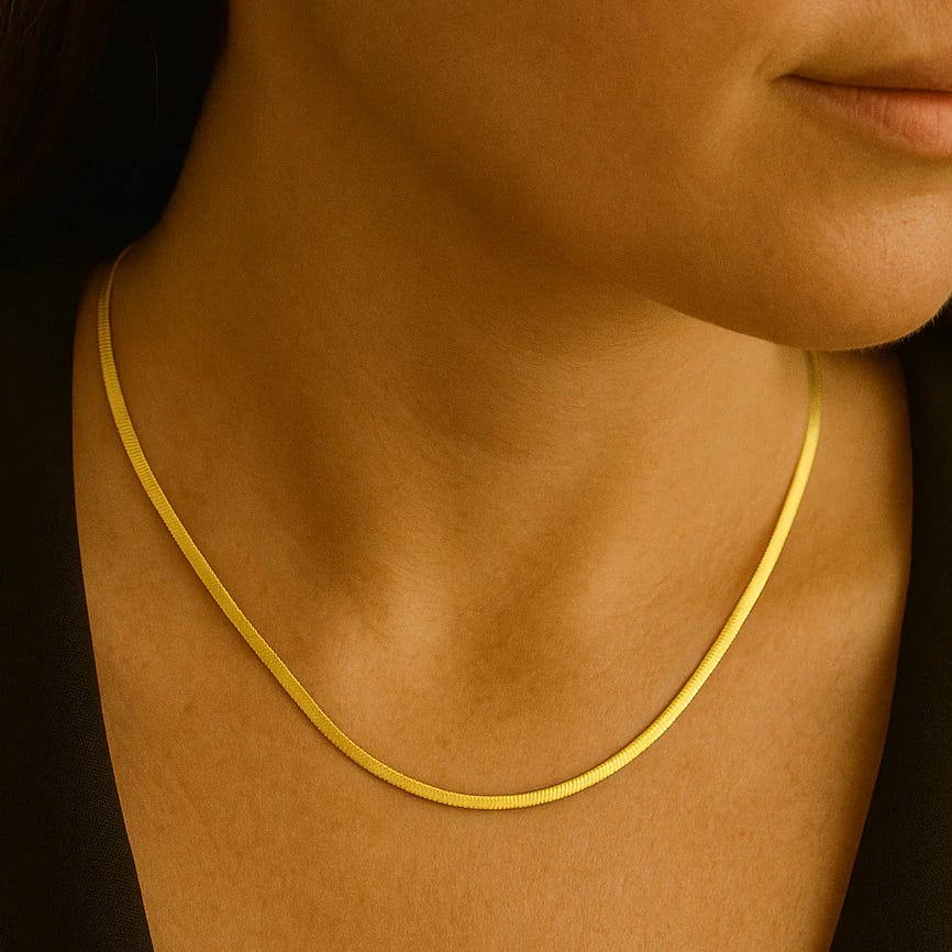 A woman is wearing a sleek, thin gold necklace close to her neck, paired with a black outfit.