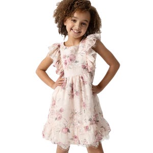 A young girl is wearing a sleeveless floral dress with ruffled shoulders and a lace hem. The dress features a light pink background with pink and green floral patterns.