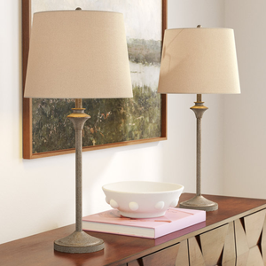 Two table lamps with beige shades and slender, textured bases are placed on a wooden console table. A white decorative bowl sits atop a pink book between the lamps.