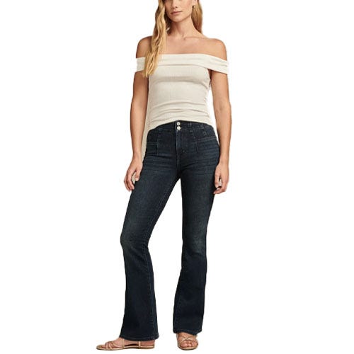 A person is wearing an off-the-shoulder white top paired with dark blue flare jeans and flat sandals.