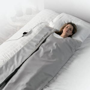 A heated weighted blanket is being used by a person lying down, with a control unit visible.