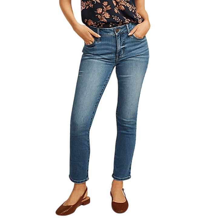 A person wearing medium-wash skinny jeans paired with brown slingback shoes and a navy blue floral top.