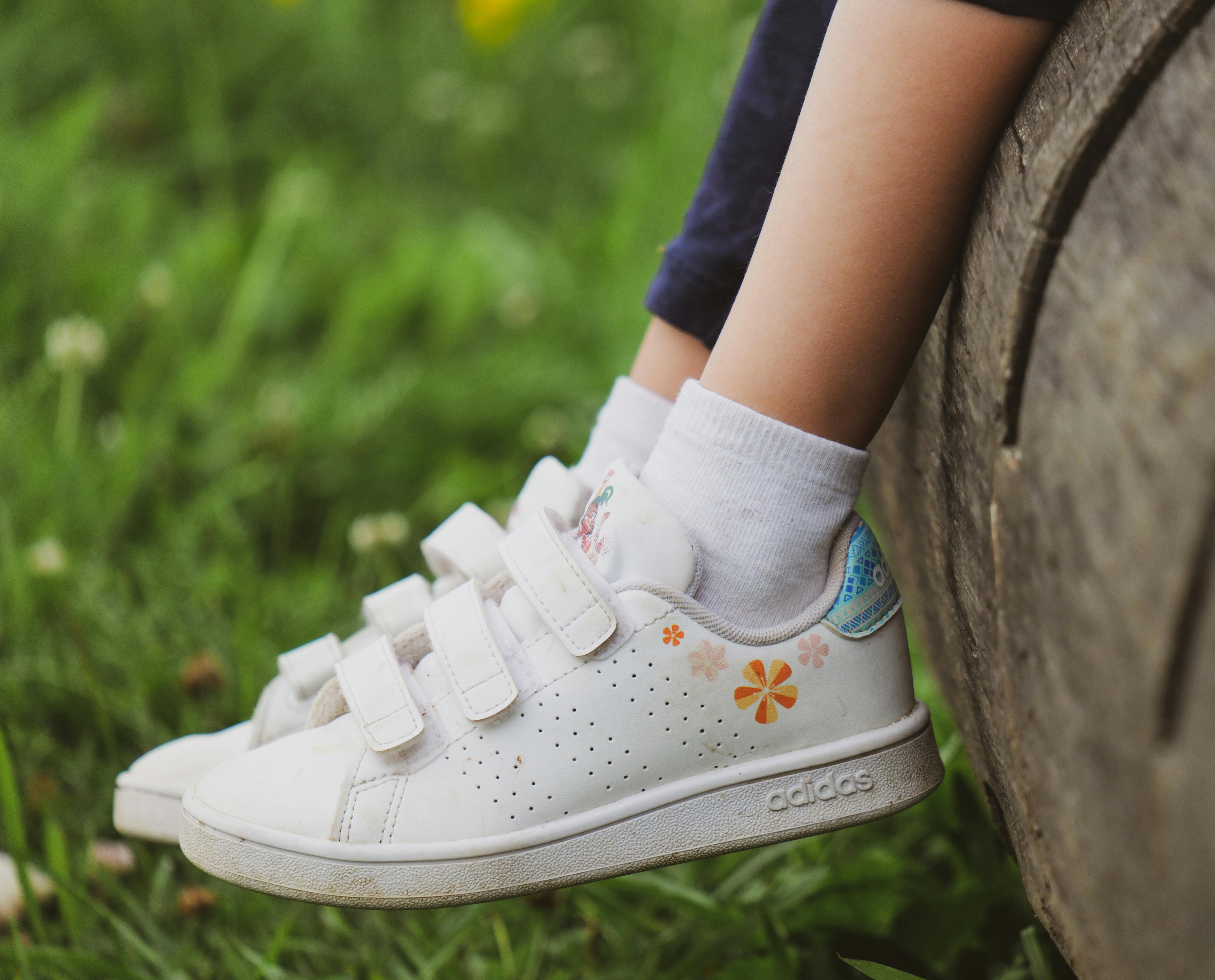 A pair of white Adidas children's sneakers with Velcro straps and floral detailing.