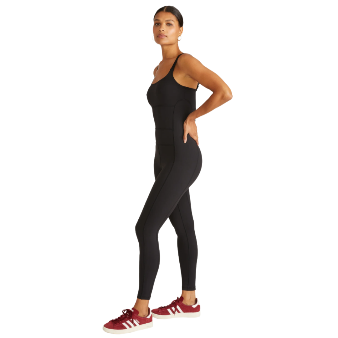 A person is wearing a black full-body athletic jumpsuit with spaghetti straps, paired with maroon Adidas sneakers.