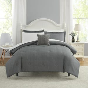 A queen-size bed is adorned with a 10-piece comforter set featuring a grey comforter, various coordinating grey and white pillows, and matching shams set in a bedroom with bright natural light.