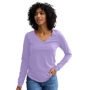 A woman wearing a long-sleeve, light purple V-neck shirt and blue jeans.