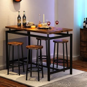 A wooden dining table set with a dark metal frame, featuring four matching stools. The table is decorated with bottles, candles, glasses, and plates, placed on a patterned rug in a cozy corner.