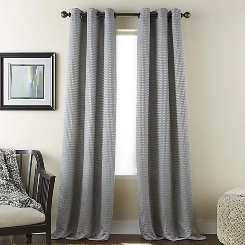 Gray curtains with a subtle checkered pattern hang from a black rod in front of a window. To the left is a chair with a textured throw, and a framed abstract painting hangs on the wall.