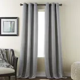 Gray curtains with a subtle checkered pattern hang from a black rod in front of a window. To the left is a chair with a textured throw, and a framed abstract painting hangs on the wall.