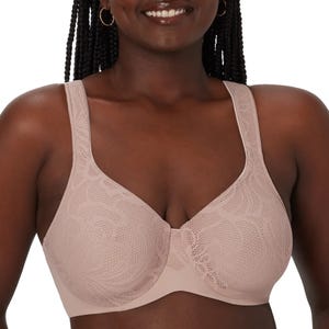A woman is wearing a nude-colored, underwire bra with textured floral patterns and wide straps.