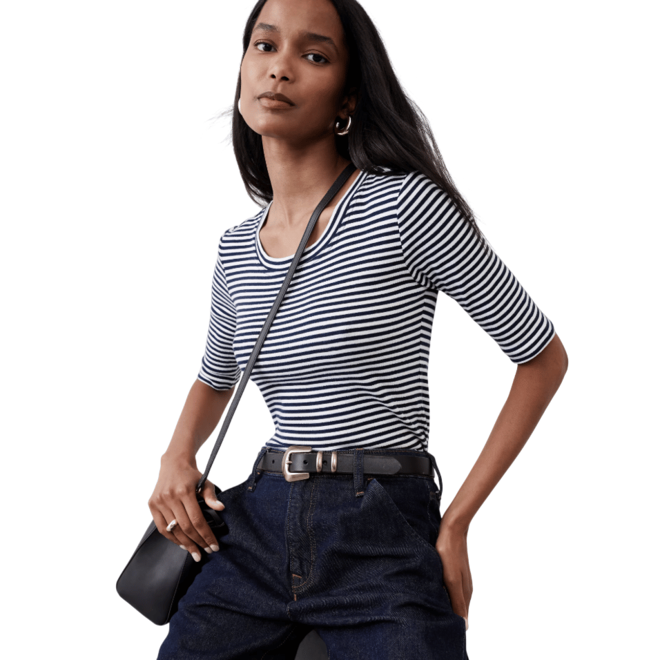 A person is wearing a navy and white striped shirt with three-quarter sleeves, dark high-waisted jeans with a black belt, holding a black shoulder bag.