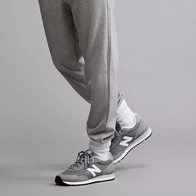 Gray New Balance 515 sneakers with white and darker gray accents, featuring a prominent 'N' logo on the side and a white midsole. The sneakers are paired with light gray sweatpants.