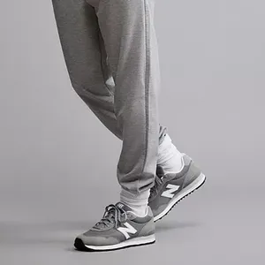 Gray New Balance 515 sneakers with white and darker gray accents, featuring a prominent 'N' logo on the side and a white midsole. The sneakers are paired with light gray sweatpants.