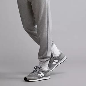 Gray New Balance 515 sneakers with white and darker gray accents, featuring a prominent 'N' logo on the side and a white midsole. The sneakers are paired with light gray sweatpants.