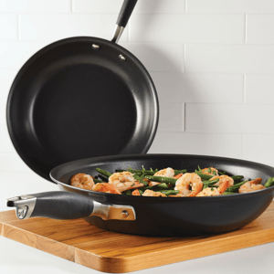 Two non-stick frying pans on a wooden board, one with sautéed shrimp and green beans.