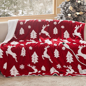 A red and white festive blanket with reindeer, trees, and snowflakes, draped over a sofa near a decorated, snow-covered Christmas tree.