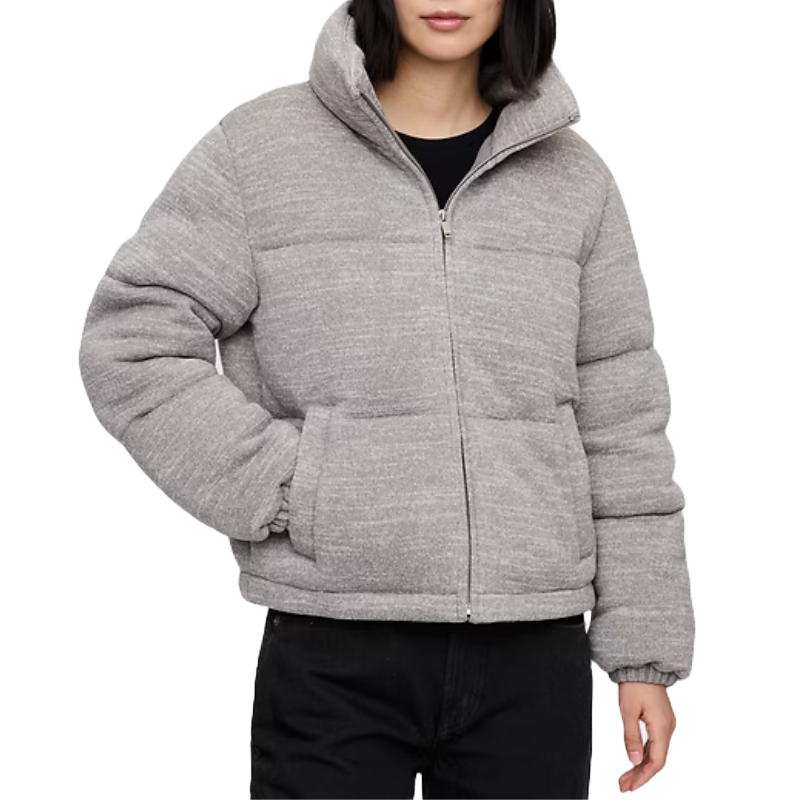 A woman is wearing a gray, zip-up puffer jacket. The jacket has a high collar, a quilted design, and elastic cuffs, offering a casual and warm fit.
