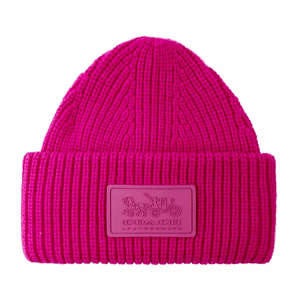 A bright pink, ribbed knit beanie with a folded cuff featuring a rectangular patch embossed with the Coach horse and carriage logo.