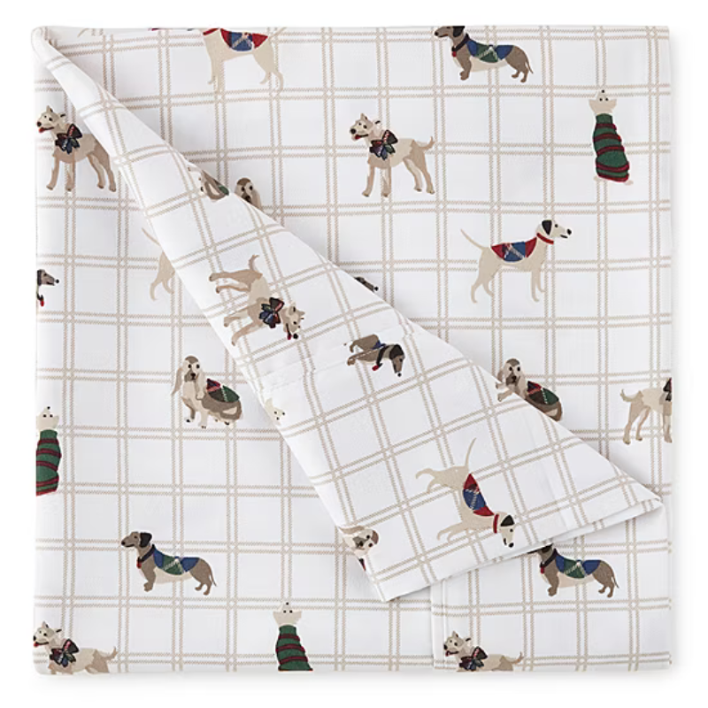 A beige grid-patterned bedsheet featuring various dogs wearing colorful sweaters.