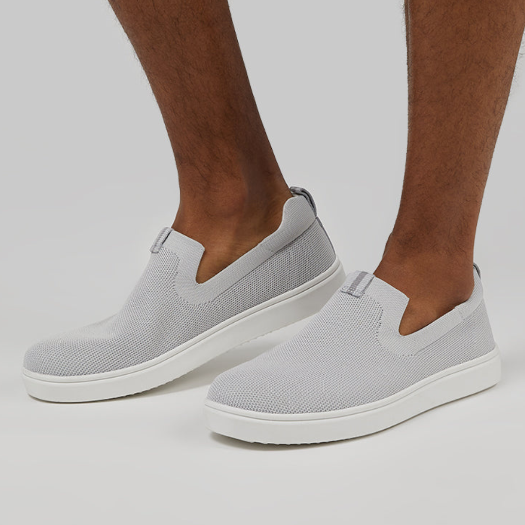 A pair of grey slip-on sneakers worn by a person.