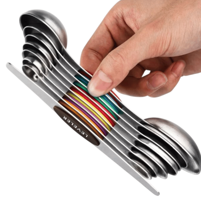 A set of stainless steel measuring spoons stacked in a compact, colorful design, held by a hand. Each spoon is marked with metric and US measurements.