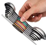 A set of stainless steel measuring spoons stacked in a compact, colorful design, held by a hand. Each spoon is marked with metric and US measurements.
