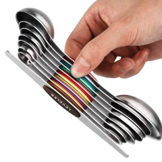 A set of stainless steel measuring spoons stacked in a compact, colorful design, held by a hand. Each spoon is marked with metric and US measurements.