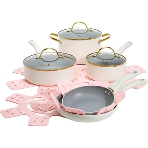 The Paris Hilton 12pc Cookware Set features cream-colored pots and pans with gold accents, glass lids, and pink protective liners. The set includes various sized frying pans, saucepans, and a pot.