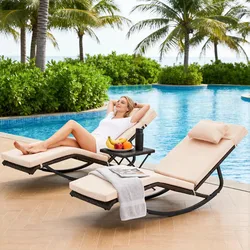 Two beige cushioned lounge chairs with black metal frames are by a pool, accompanied by a small table holding a towel, magazine, fruit, and a thermos.