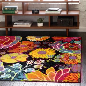 A colorful floral-patterned rug lies on dark wood flooring in front of a mid-century modern wooden shelf, which holds books, a camera, a small plant, and a decorative trunk.