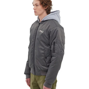 The Bench DNA Bomber Jacket is gray with a sleek design featuring a zip-up front, a zippered sleeve pocket, and two front pockets. It is worn over a gray hoodie, complementing the look with olive green pants.