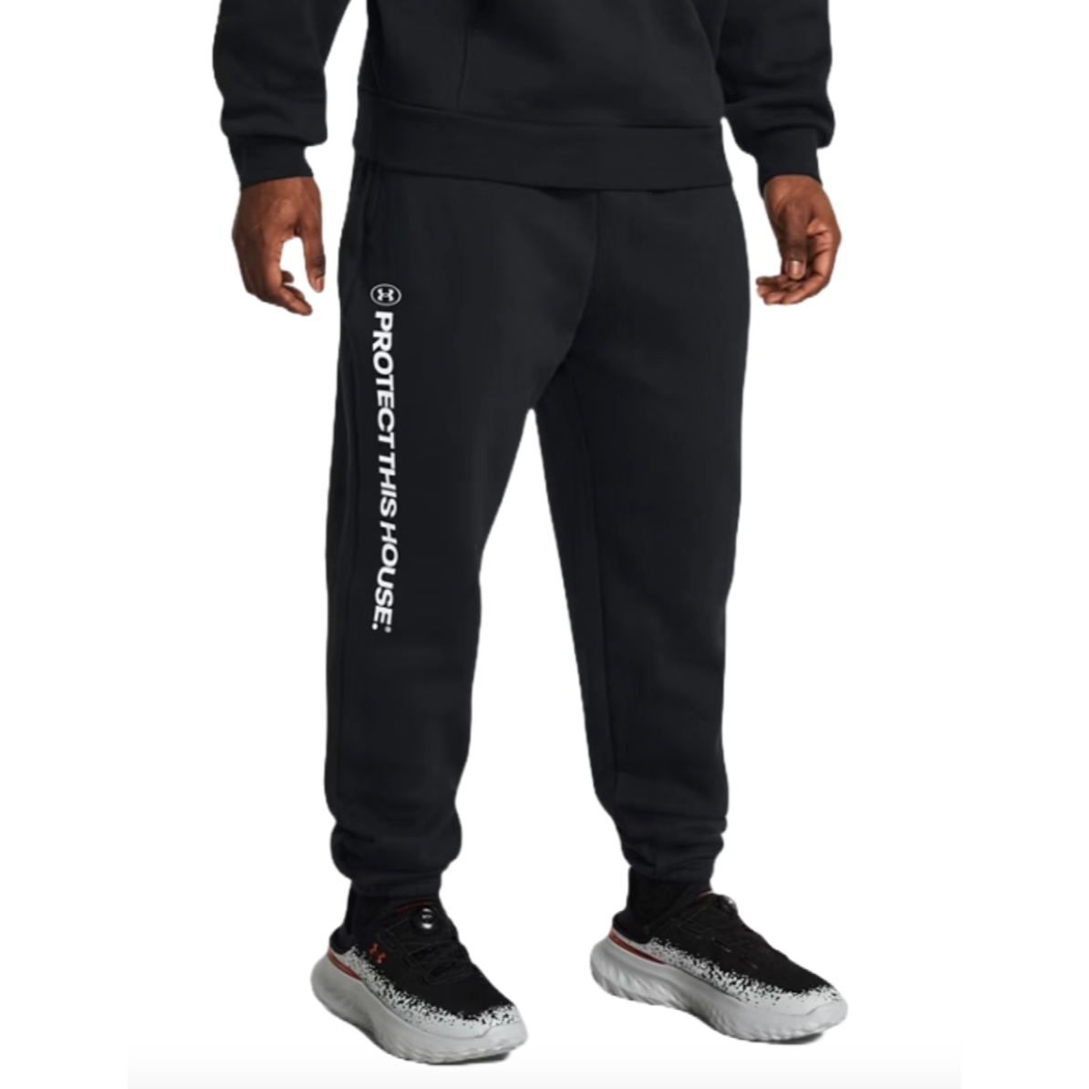 Black joggers with the Under Armour logo and \“PROTECT THIS HOUSE\“ printed vertically on the left leg. They feature a relaxed fit with ribbed cuffs, a comfortable waistband, and are paired with light-colored running shoes.