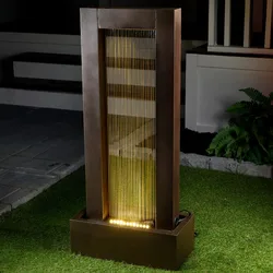 Modern outdoor LED-lit water feature with vertical streams in a rectangular frame, placed on artificial grass near a patio area.