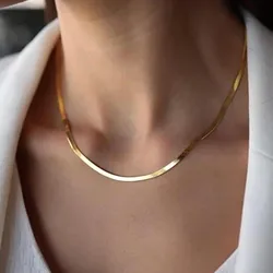 A person is wearing a simple, elegant gold necklace with a smooth, curved design, complemented by a white blouse and blazer.