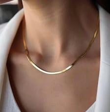 A person is wearing a simple, elegant gold necklace with a smooth, curved design, complemented by a white blouse and blazer.