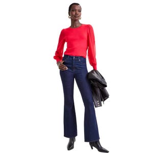 Dark blue high-rise flare jeans, fitted through the hips and thighs, with a slight flare at the bottom. The model pairs them with a red long-sleeve top and black boots, holding a black jacket.