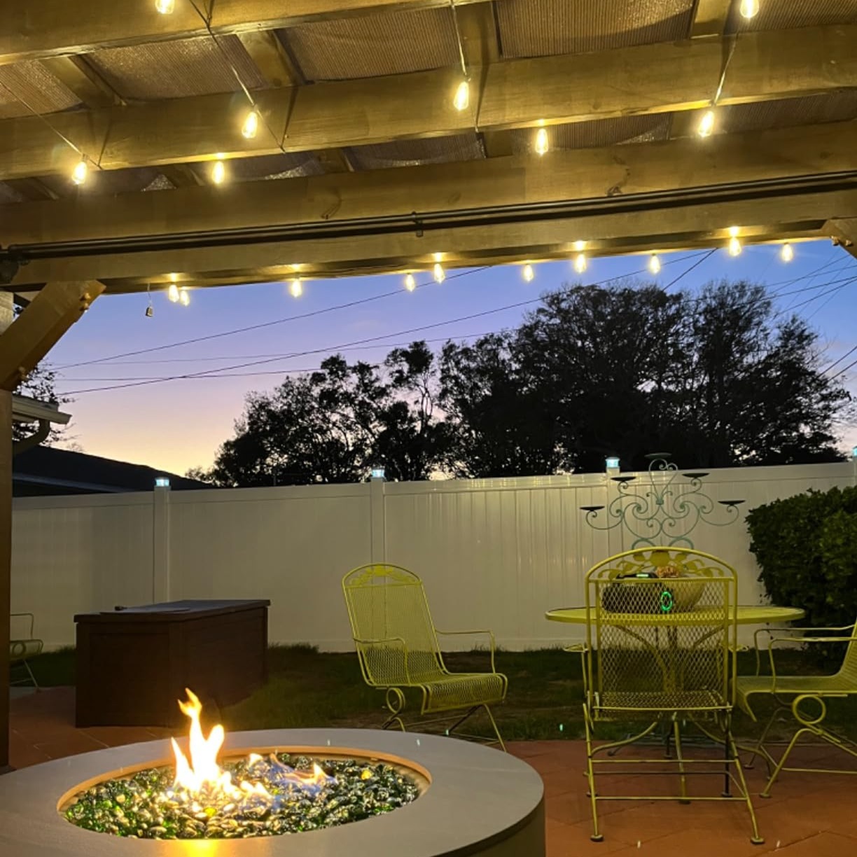 Outdoor string lights, a fire pit with visible flames, and a yellow patio furniture set.